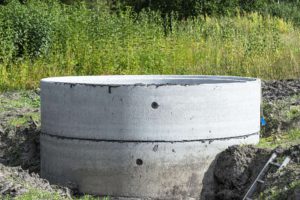 Concrete septic tank made of several rings with an orange drainpipe at the bottom.