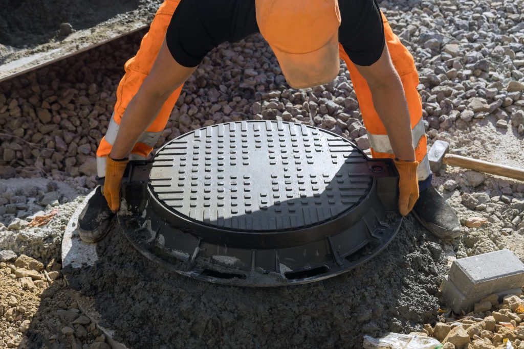 Installing cast iron sewer hatch on a concrete base of installation of water main sewer well in the